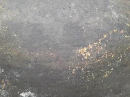 A rough, weathered surface with dark gray and brownish patches, showing signs of wear, rust, or natural aging over time. photo