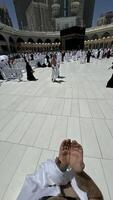 A bald man poses for a photo in front of the Kaaba at noon after performing Umrah at Masjid al-Haram, Mecca. A sacred Islamic pilgrimage in the heart of the holy mosque under the bright sunlight.