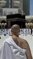 Former Sinner man who converted to Islam, with a large tattoo on his back and arm, praying with devotion in Makkah while gazing at the sacred Kaaba, embracing his new faith with deep spiritual photo
