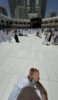 A bald man poses for a photo in front of the Kaaba at noon after performing Umrah at Masjid al-Haram, Mecca. A sacred Islamic pilgrimage in the heart of the holy mosque under the bright sunlight.