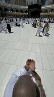 A bald man poses for a photo in front of the Kaaba at noon after performing Umrah at Masjid al-Haram, Mecca. A sacred Islamic pilgrimage in the heart of the holy mosque under the bright sunlight.