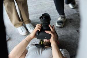 A photographer lies on the floor, capturing a heartfelt shot of a group of models embracing each other, showcasing their natural connection and joy in an intimate and creative moment photo