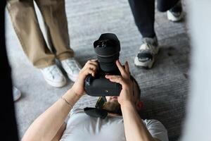 A photographer lies on the floor, capturing a heartfelt shot of a group of models embracing each other, showcasing their natural connection and joy in an intimate and creative moment photo