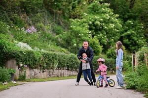A group of children, including a boy and girl playing with a ball and their young friend riding a bike, enjoying a fun filled day in a natural outdoor setting photo