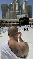 Former Sinner man who converted to Islam, with a large tattoo on his back and arm, praying with devotion in Makkah while gazing at the sacred Kaaba, embracing his new faith with deep spiritual photo