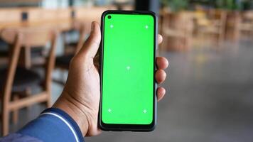 main en portant téléphone intelligent avec vert écran dans moderne café réglage video