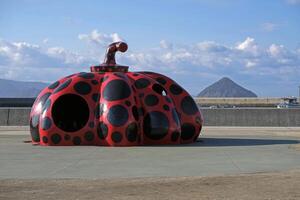 Naoshima, Japan - 12 January 2025 - Kusama Yayoi's Red Pumpkin sculpture in the port of Naoshima, Japan, with Ozuchi island in the background photo