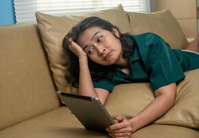 Asian women lying down on the sofa watching a movie online digital tablet and shocked expression face, using social media, reading e-book online relaxing vacation lifestyle concepts at home photo