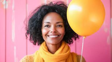 Beautiful African American woman smiling holding yellow balloon on pink background. Congratulations on holiday and birthday. photo