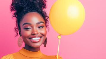 Beautiful African American woman smiling holding yellow balloon on pink background. Happy holiday and birthday greetings. photo