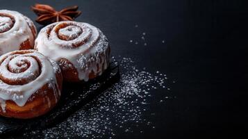 Three warm and delicious cinnamon rolls glazed to perfection on a striking black surface ready for sweet indulgence photo