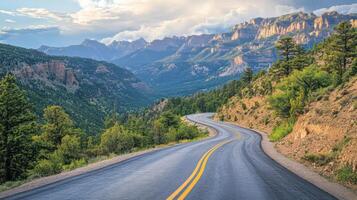 Mountain road winds through trees. Sunlight on peaks and green hills. Asphalt path curves. Sky and clouds above scenic view. Landscape picture. photo