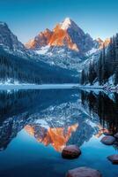 Snowy mountain reflects in a calm lake. Winter scene with rocks in the water. Trees line the shore of the still, peaceful lake. photo