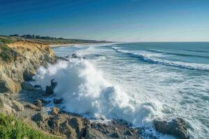 Ocean waves crash on rocky cliff. Water splashes on coast under bright sun and blue sky. Coastal scene with beach and green plants. photo