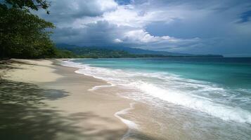 Tropical beach view. Sea waves washing sand. Trees beside shore. Cloudy sky over blue water and green mountains. Peaceful ocean coast scene. photo