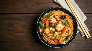 Chinese noodles with chicken and vegetables in a bowl on a wooden table top view photo