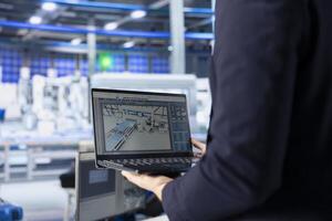 Engineer in photovoltaics factory using tracking software on laptop to diagnose malfunctioning systems. Solar panels manufacturing plant worker uses notebook to reduce downtime photo