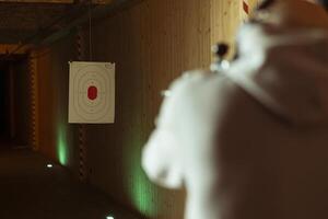 Man in shooting range using handgun to hit paper targets with ammunition. Close up shot of client at indoor firing range facility shooting bullseyes, enjoying using weapons during leisure time photo