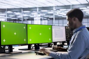 Engineer in server hub ensuring data remains shielded from potential threats using chroma key PC. Employee safeguarding data center against hackers with multi monitor mockup computer setup photo