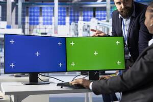 Photovoltaics factory team leader and expert finetuning system settings on green screen PC. Manager works with engineer on solar panels plant assembly lines configuration using chroma key computer photo