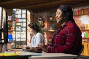 Cheerful call center operator talking in headset microphone, helping customers regain access to accounts and devices. Jolly customer center worker assisting clients needing help resetting password photo