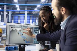 Solar panels plant business partners looking over factory energy consumption on computer. Man and woman in photovoltaics facility managing manufacturing resources using PC photo