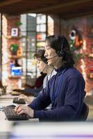 Call center agent in office helping customers by answering questions, solving their issue. Man in customer support workspace in front of PC using headset mic to talk with clients photo