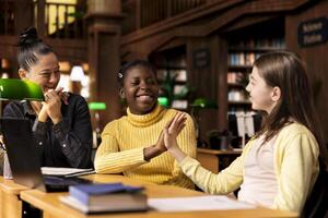 Pleased happy schoolgirls sharing a high five during private lessons with tutor in the library, finishing their team project work. Elementary school pupils feeling satisfied with academic progress. photo