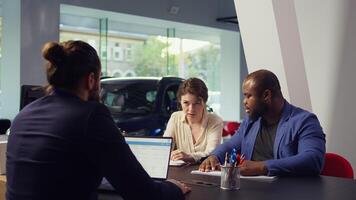 Customers in dealership completing necessary payment paperwork related to car sale, collaborating with finance and insurance departments to ensure smooth transaction, camera B photo
