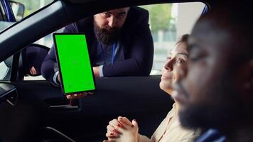 Showroom salesman showing stat charts on green screen tablet to clients after test drive. Dealership agent showing vehicle driving metrics graphs on chroma key device to couple, camera B photo