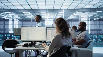 System admin working in diverse computer network security data center workplace, ensuring optimal performance. Worker monitoring energy consumption across server racks, camera B photo