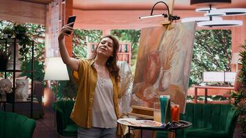 In modern atelier, artist filming rustic artwork painting with smartphone, social media branding. Recording and taking pictures of colorful canvas with watercolor piece, self promotion. Camera B. photo
