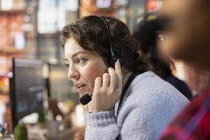 Customer service employee talking in headset mic, tracking support ticket in dedicated company software on PC. Call center worker creating support ticket for customer calling to solve issue photo