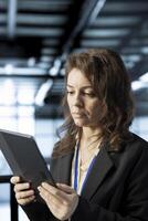 Woman in data center operating tablet, analyzing metrics, optimizing storage volumes, reviewing network paths, validating virtualization settings, ensuring seamless operations photo