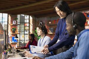 Call center senior manager going over job description file with employee at PC desk. Asian customer support onboarding specialist explaining tasks to intern accommodating with job photo