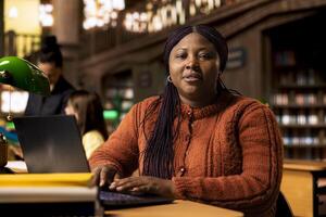 Portrait of african american librarian working with academic resources and learning materials within the public library database. Smiling woman focused on her educational profession. photo