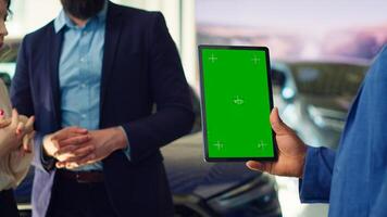 Salesman using green screen tablet to present car addons options to clients, trying to sway them make purchase. Showroom agent offers extended warranty to customers, holding mockup device, camera A photo