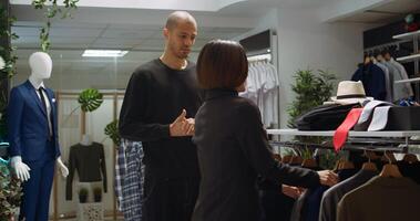 Fashion expert worker selecting a variety of trendy items for client, helping him to change in the dressing room. Young man trying on clothes from the new collection, showroom. Camera B. photo