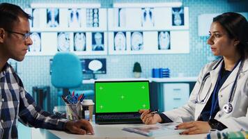 Indian physician consulting a patient in medical facility next to chroma key, using modern tech for scan interpretation and results. Medic giving professional advice based on records. Camera B. photo