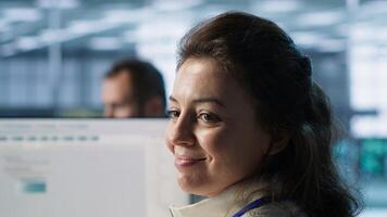 Smiling IT engineer in data center using PC to find misconfigurations affecting rackmounts. Cheerful woman checking servers bottlenecks leading to sluggish data transfer rates, camera A close up photo