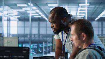Programmer requesting help from manager while working on computer in data center, monitoring hardware energy consumption. Team leader overseeing IT expert checking for system failures, camera A photo