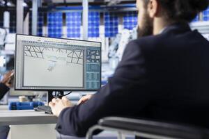 Photovoltaics factory manager in office visualizing solar cells designs with 3D software on PC. Solar panels plant technician sitting down at desk doing computer simulations in CAD program photo