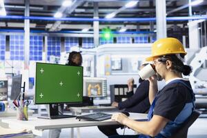 Solar panels plant engineer drinking coffee doing quality control using green screen computer. Photovoltaics factory specialist enjoying beverage calibrating robotic arms on mockup PC photo