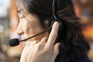 Call center staff member using headphones mic to answer technical inquiries about hardware issues. Knowledgeable Asian worker doing customer support job using PC to troubleshoot problems, close up photo