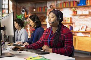 Teamworking call center colleagues in office helping customers by answering questions. Team of agents in customer support workplace in front of PC using headset mic to talk with clients photo