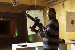 Portrait of shooting range client reloading rifle, preparing to shoot targets during leisure time. Man at indoor shooting ground facility loading semiautomatic weapon, wearing protection goggles photo