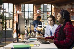 Portrait of customer service employee next to coworker tracking support ticket in dedicated company software on PC. Call center worker at office desk creating support ticket for customer calling photo