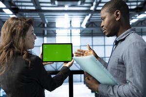 Admins in data center using mockup tablet, observing analytics, reviewing infrastructure health. Server hub IT coworkers discussing, using chroma key device, adjusting system parameters photo