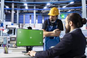Photovoltaics factory engineering team using green screen PC to improve solar panels assembly processes. Coworkers use chroma key computer to calibrate equipment for precise solar cells manufacturing photo
