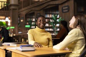 Adorable teenagers having fun laughing and gossiping together in a public library, joking around and feeling happy with their friendship. Diverse scholars enjoying a discussion after classes. photo